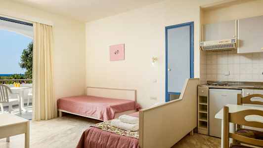 Interiör av ett hotellrum med två enkelsängar, ett litet kök och en balkong med utsikt. (AI-genererad text)