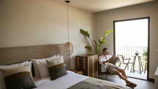 Ett hotellrum med en bäddad dubbelsäng, modern inredning, och en balkong med utemöbler samt grönska. (AI-genererad text)