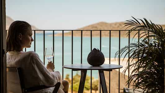 En person sitter på en balkong och håller ett glas med utsikt över havet. (AI-genererad text)