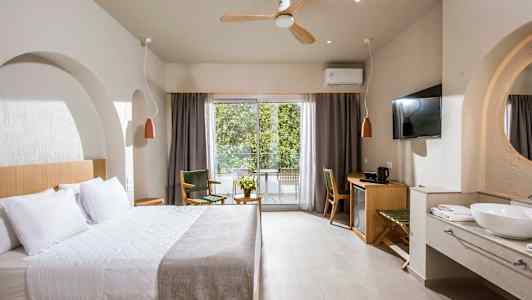 Ett hotellrum med en stor säng, sittmöbler, skrivbord och en balkong med utsikt mot grönska. (AI-genererad text)