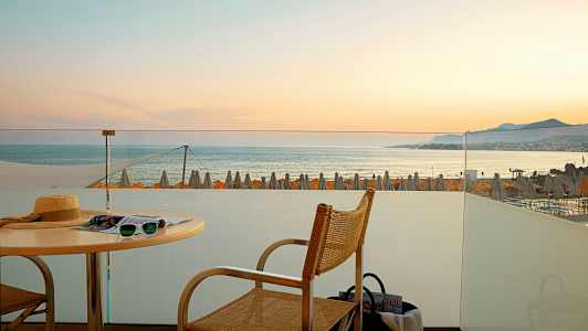 Utsikt från en terrass mot havet med solnedgång och strandparasoller i bakgrunden. (AI-genererad text)