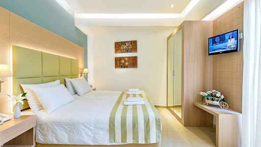 Ett hotellrum med en stor säng, dekorerat med randigt sängöverkast och vita kuddar. På väggen finns konst med blommotiv, och till höger står en TV samt en liten möbel med blommor. (AI-genererad text)