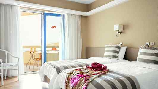 Ett hotellrum med två enkelsängar, randiga sängkläder och en dörr till en balkong. (AI-genererad text)