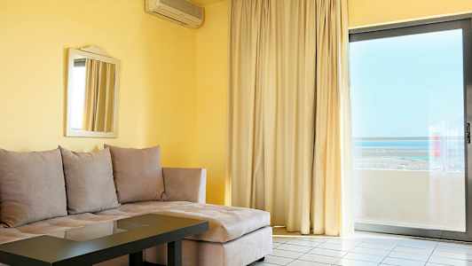 Ett vardagsrum med beige hörnsoffa, glasbord, spegel på väggen och stor fönsterdörr mot både gardiner och utsikt. (AI-genererad text)