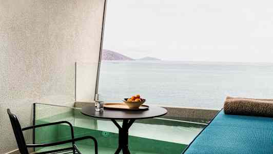 En terrass med bord, stol och en sittplats vid en liten pool med utsikt över havet. (AI-genererad text)