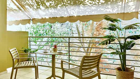 En terrass med ett bord och två stolar nära ett räcke, dekorerad med växter. (AI-genererad text)