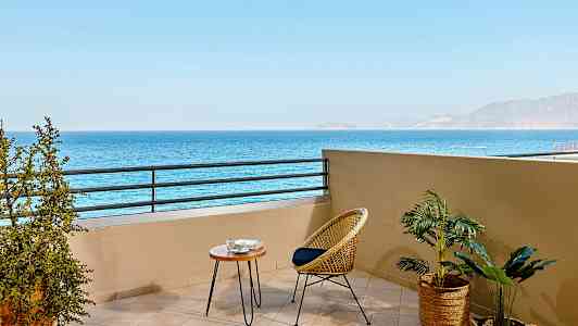 Balkong med utsikt över havet, möblerad med en rottingstol och ett litet bord. (AI-genererad text)