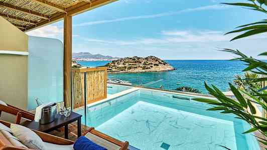 Utsikt över en pool på en terrass med hav och klippiga kullar i bakgrunden. (AI-genererad text)