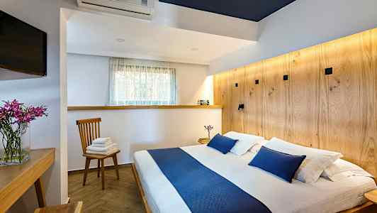 Bild av ett sovrum med en dubbelsäng och blå detaljer, ett träbord, en stol med handdukar och en TV. (AI-genererad text)