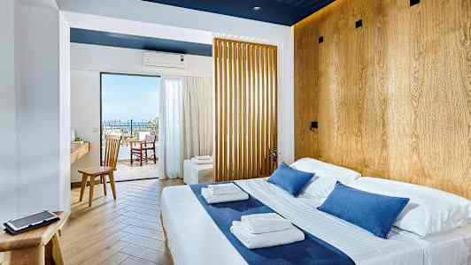 Ljust hotellrum med dubbelsäng och trädetaljer, utsikt mot balkong och hav. (AI-genererad text)