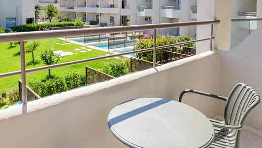 Utsikt från en balkong med utsikt över en grönskande trädgård och poolområde. (AI-genererad text)