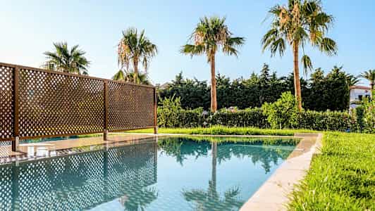 Utomhuspool med speglade palmer och staket. (AI-genererad text)