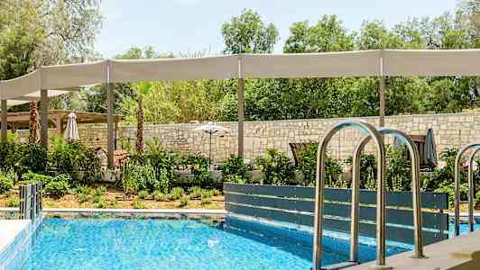 Utomhuspool med omgivande grönska och sittplatser med skuggtak. (AI-genererad text)