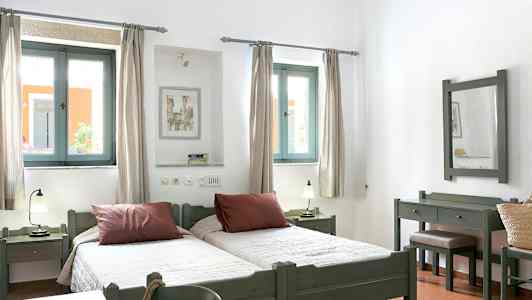 Bild av ett ljust sovrum med två enkelsängar, fönster med ljusinsläpp och möbler i trä. (AI-genererad text)