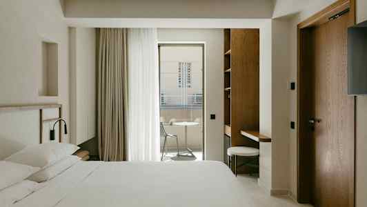 Ett hotellrum med en dubbelsäng, skrivbord och balkong med utemöbler. (AI-genererad text)