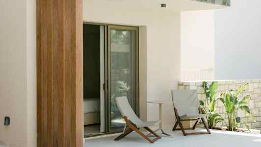 En terrass med två sittstolar, ett litet bord och gröna växter intill en glasad dörr. (AI-genererad text)