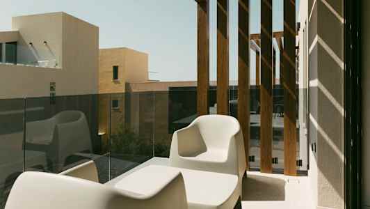 Två vita stolar och ett bord på en balkong med glasräcke och träpaneler. (AI-genererad text)