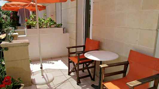 Utomhusterrass med två orangefärgade stolar och ett vitt bord under ett parasoll. (AI-genererad text)