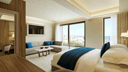 Modern hotellrum med en dubbelsäng, sittgrupp och stora fönster med utsikt över havet. (AI-genererad text)