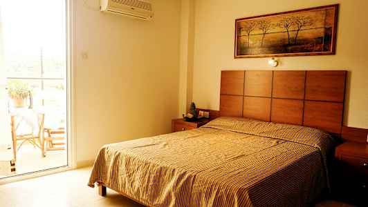 Ett sovrum med en säng, ett nattduksbord, och en tavla på väggen; bredvid finns en öppen balkongdörr. (AI-genererad text)