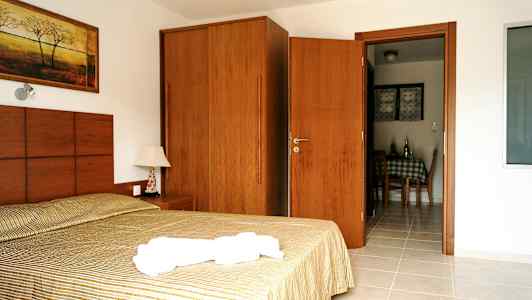 Bild av ett hotellrum med en säng, ett nattduksbord, en garderob och dörr som leder till matsalsområdet. (AI-genererad text)