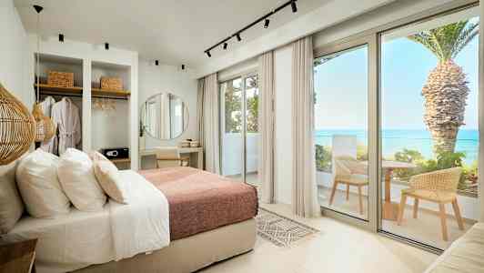 Modernt hotellrum med säng, skrivbord, garderob och balkong med havsutsikt. (AI-genererad text)