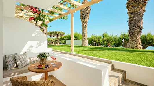 Uteservering med bord och stolar i en trädgård med palmer och havsutsikt. (AI-genererad text)