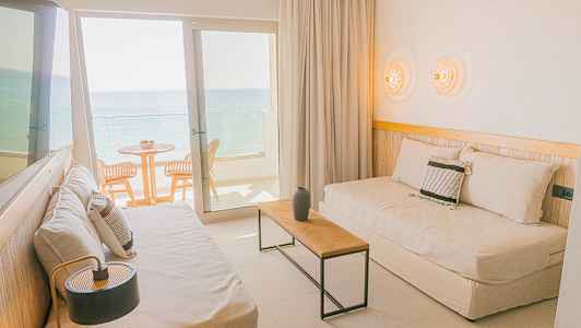 En hotellrum med sittmöbler och balkong som vetter mot havet. (AI-genererad text)