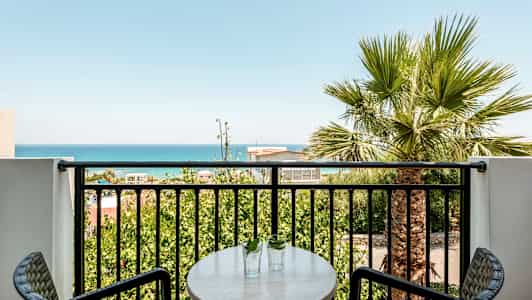 En balkong med utsikt över havet och gröna träd. (AI-genererad text)