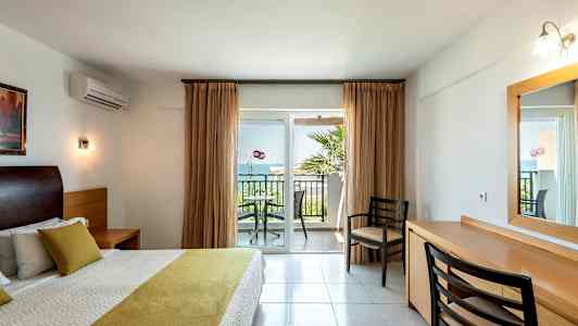 Sovrum med dubbelsäng och utsikt mot en balkong med stolar och bord. (AI-genererad text)