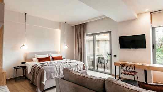 Ett modernt hotellrum med säng, soffa, skrivbord, TV och en balkong med utsikt. (AI-genererad text)