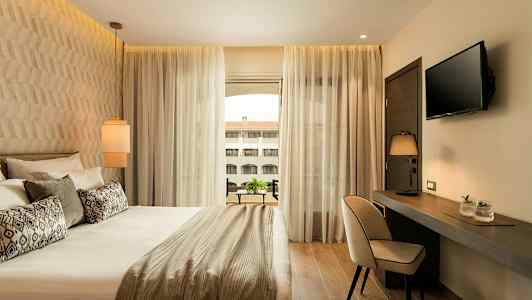 Modern hotellrum med säng, skärm, och skrivbord med lampa. (AI-genererad text)