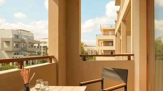 En balkong med bord, stol och utsikt över moderna byggnader. (AI-genererad text)