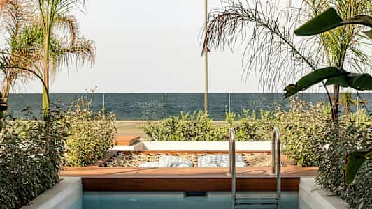 En liten pool med en träträdgård bredvid, utsikt mot ett hav och glasräcke. (AI-genererad text)