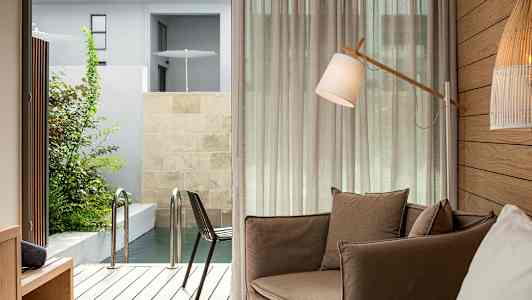 Ett rum med en brun fåtölj, en golvlampa och utsikt mot en terrass med pool. (AI-genererad text)