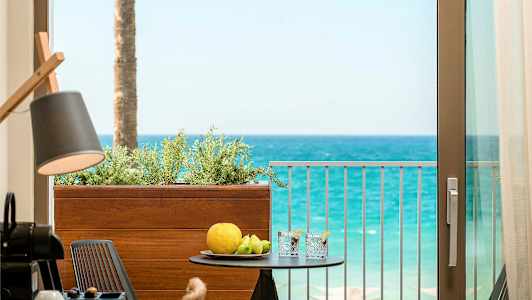 Utsikt från en balkong mot havet med ett bord som har frukter och drycker på sig. (AI-genererad text)