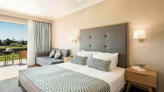 Hotellrum med dubbelsäng och sittgrupp, samt utgång till terrass med naturutsikt. (AI-genererad text)