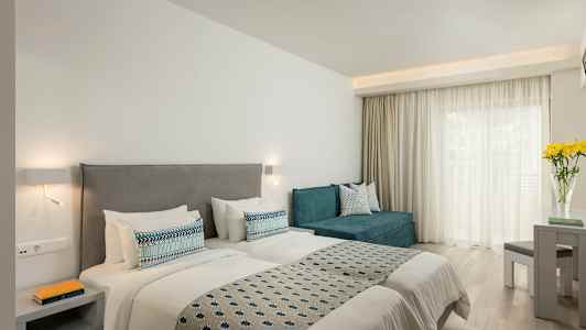 Ett hotellrum med två enkelsängar, en soffa, ett bord och blommor på ett bord vid ett fönster. (AI-genererad text)