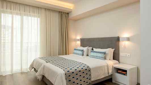 Dubbelrum med en grå huvudgavel, vita sängkläder och blåmönstrade kuddar och överkast, belyst av vägglampor. (AI-genererad text)