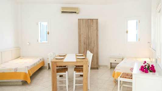 Ett ljust rum med två enkelsängar, ett matbord med stolar och en garderob. (AI-genererad text)