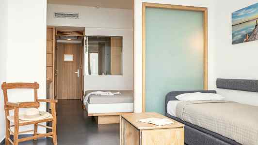 Ett hotellrum med två sängar, en stol och ett bord. (AI-genererad text)