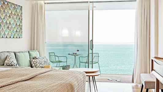 Ett sovrum med havsutsikt genom stora glasdörrar som leder till en balkong. (AI-genererad text)