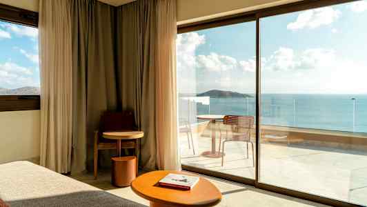 Modernt hotellrum med stora glasdörrar som vetter mot en balkong med havsutsikt. (AI-genererad text)