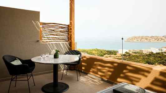 En terrass med ett bord, stolar och utsikt över havet och en liten ö. (AI-genererad text)