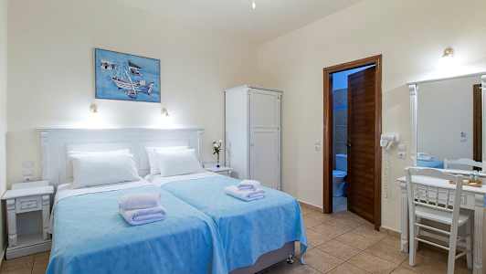 Ett hotellrum med två enkelsängar klädda med blå överkast och vita kuddar, en garderob, ett skrivbord med spegel och ett badrum med öppet dörr. (AI-genererad text)