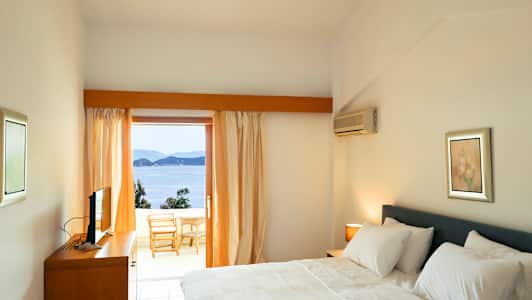 Hotellrum med en dubbelsäng och utsikt över havet från en balkong. (AI-genererad text)