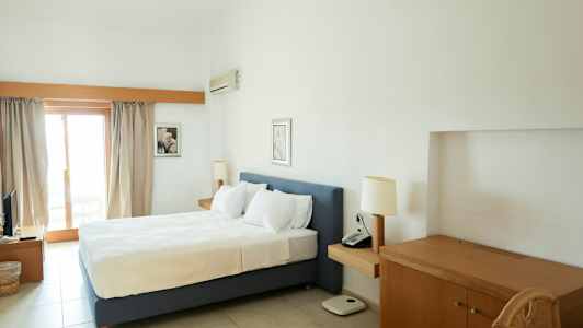 Ett hotellrum med en dubbelsäng, skrivbord och balkongdörr. (AI-genererad text)