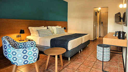 Ett hotellrum med en dubbelsäng, fåtölj, bord och skrivbord. (AI-genererad text)