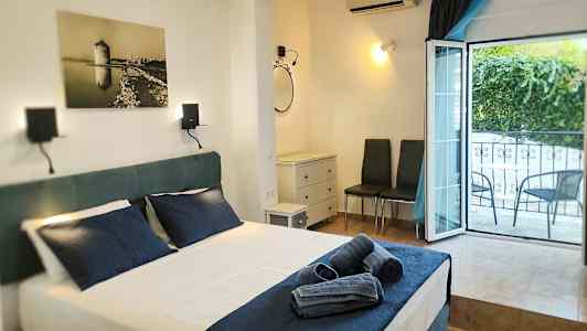 Ett hotellrum med en bäddad säng och mörkblå lakan, ett öppet fönster mot balkongen, och möbler inklusive två stolar och en byrå. (AI-genererad text)