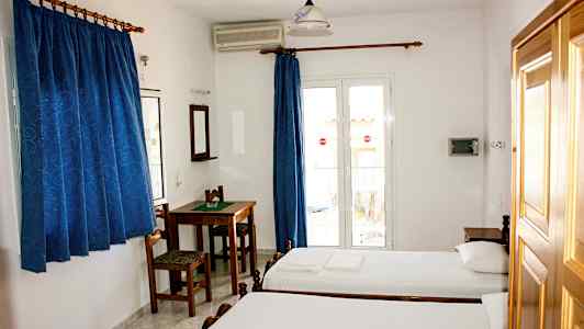 Ett hotellrum med två enkelsängar, ett bord med stolar, blå gardiner och en balkongdörr. (AI-genererad text)